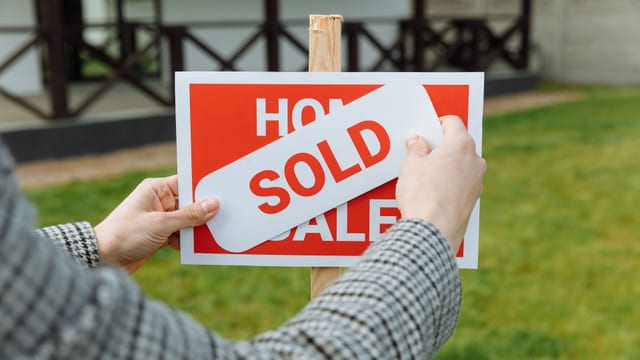 A realtor placing a SOLD sign on a real estate listing board in front of a house
